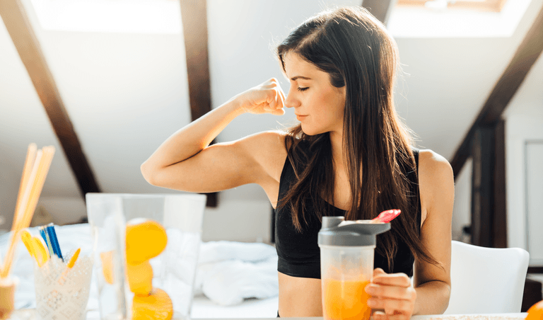 A girl holds a BCAA drink and looks at her biceps