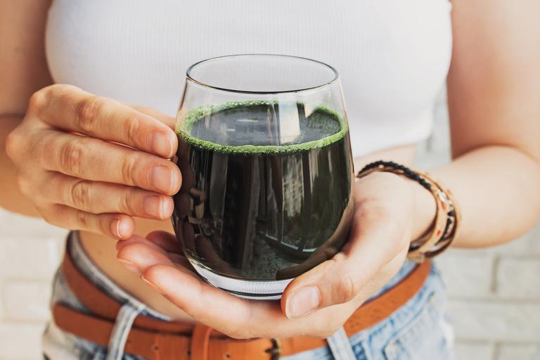 A girl holding a glass with diluted greens powder